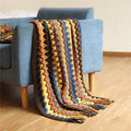Blue knitted acrylic blanket with striped pattern and fringe, draped over a sofa