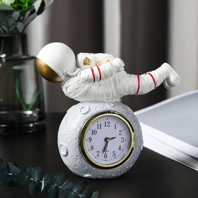 Astronaut resin clock trinket decoration in gold finish on a wooden desk with a bookshelf in background
