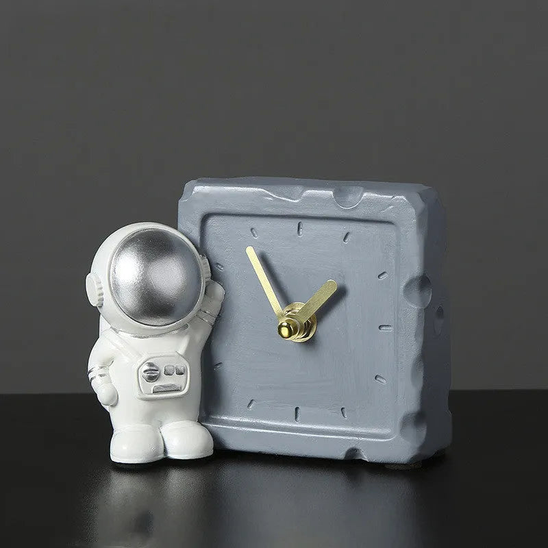 Astronaut resin clock trinket decoration in gold finish on a wooden desk with a bookshelf in background