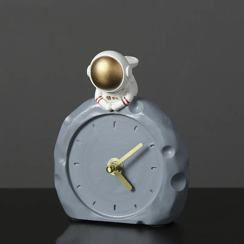 Astronaut resin clock trinket decoration in gold finish on a wooden desk with a bookshelf in background