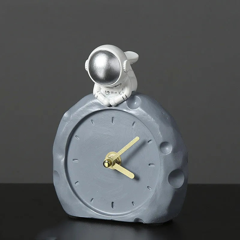 Astronaut resin clock trinket decoration in gold finish on a wooden desk with a bookshelf in background