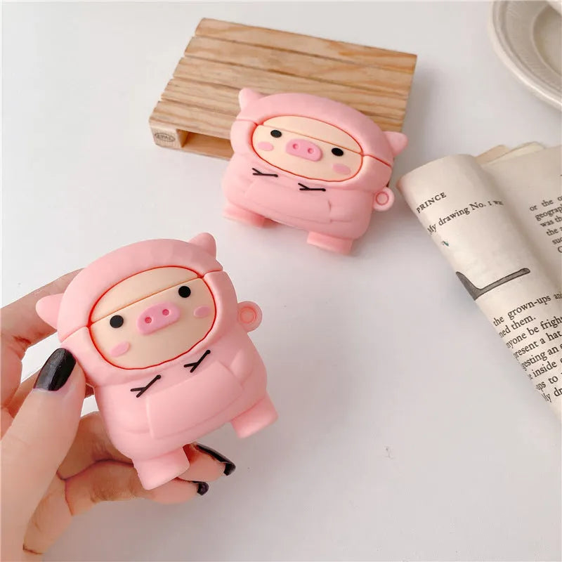 Rose pink silicone AirPods case cover with a cartoon pig in a sweater design and a silver keychain hook.