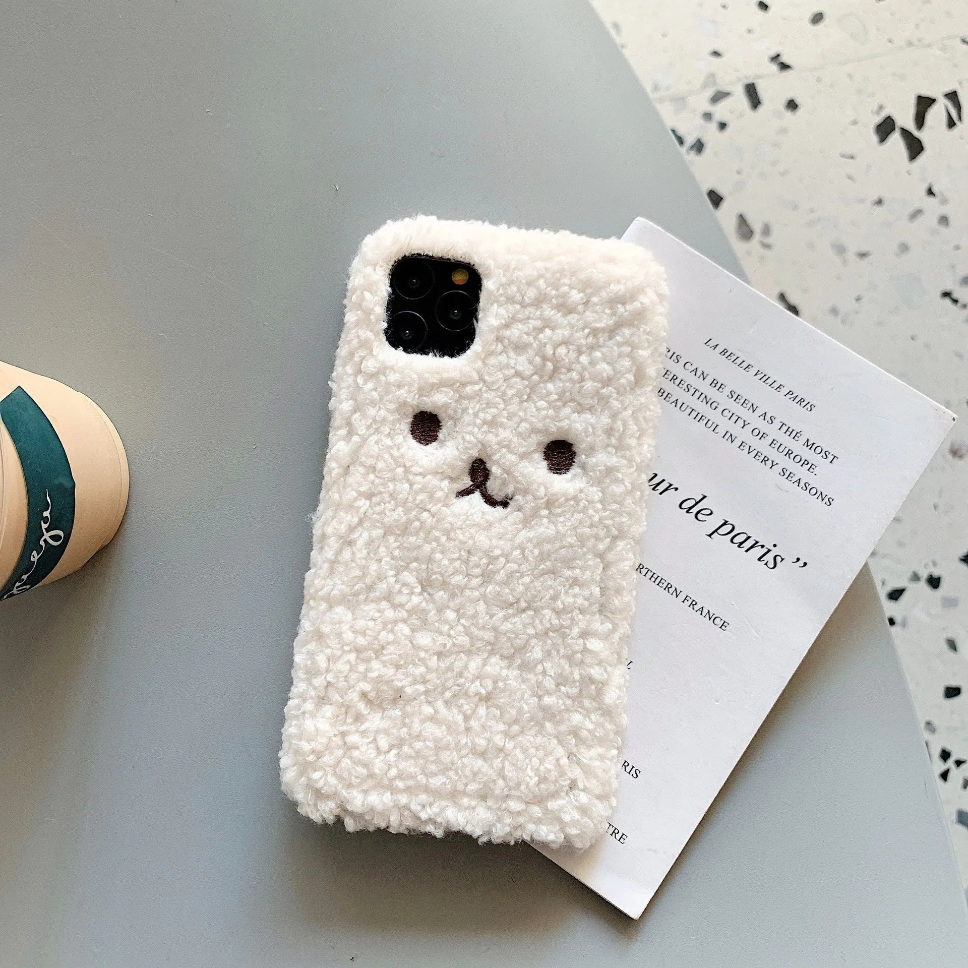 Brown embroidered plush cartoon bear face on a flexible iPhone phone case.