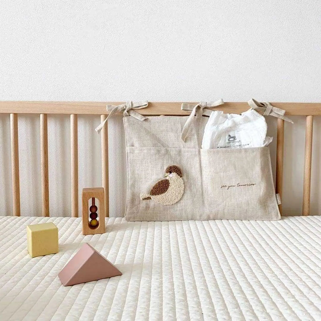 Khaki cotton linen hanging storage bag with multiple pockets mounted beside a bed.