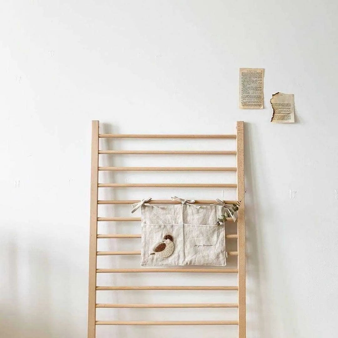 Khaki cotton linen hanging storage bag with multiple pockets mounted beside a bed.