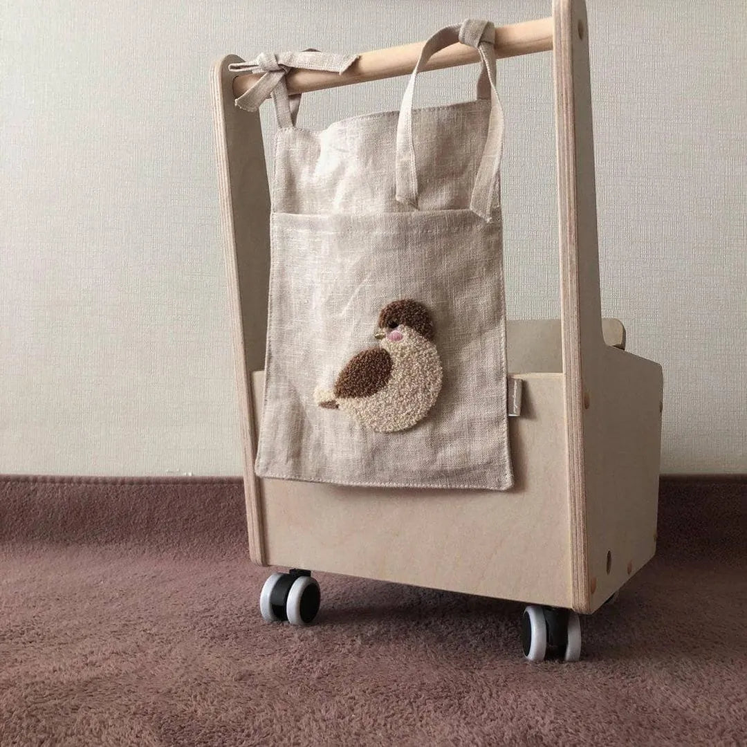 Khaki cotton linen hanging storage bag with multiple pockets mounted beside a bed.