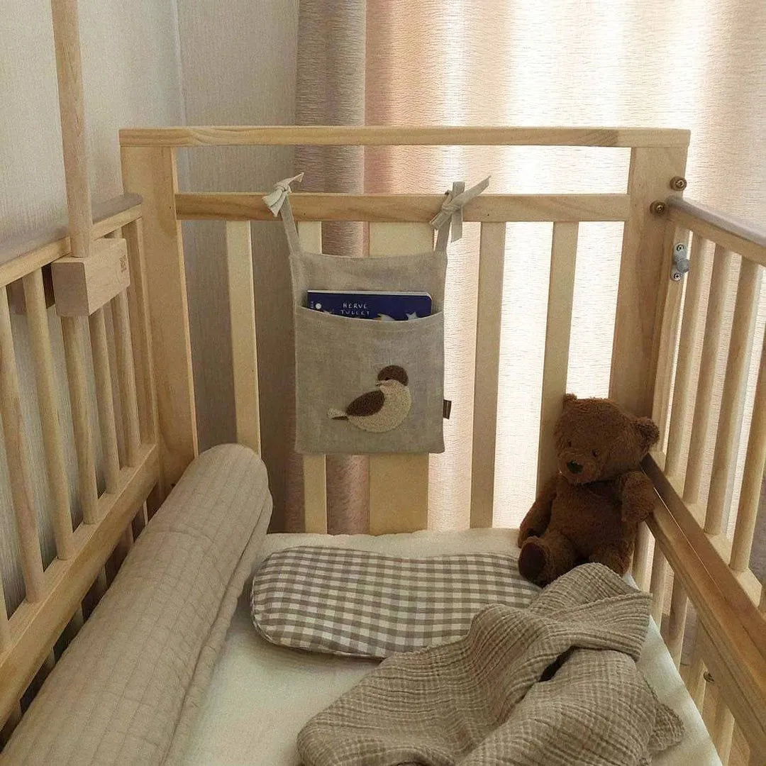 Khaki cotton linen hanging storage bag with multiple pockets mounted beside a bed.