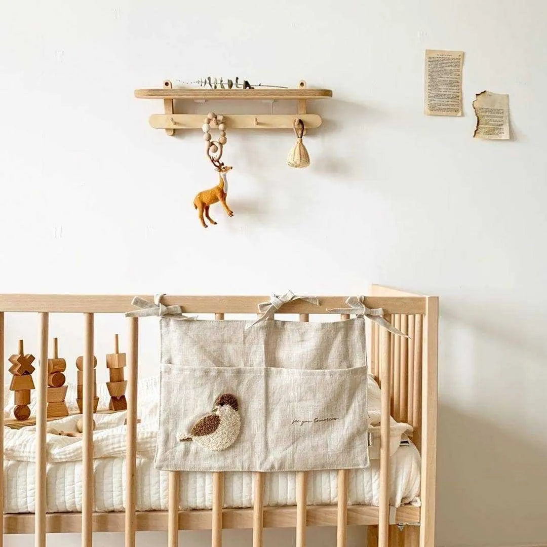 Khaki cotton linen hanging storage bag with multiple pockets mounted beside a bed.