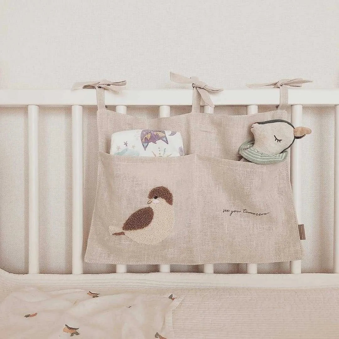 Khaki cotton linen hanging storage bag with multiple pockets mounted beside a bed.
