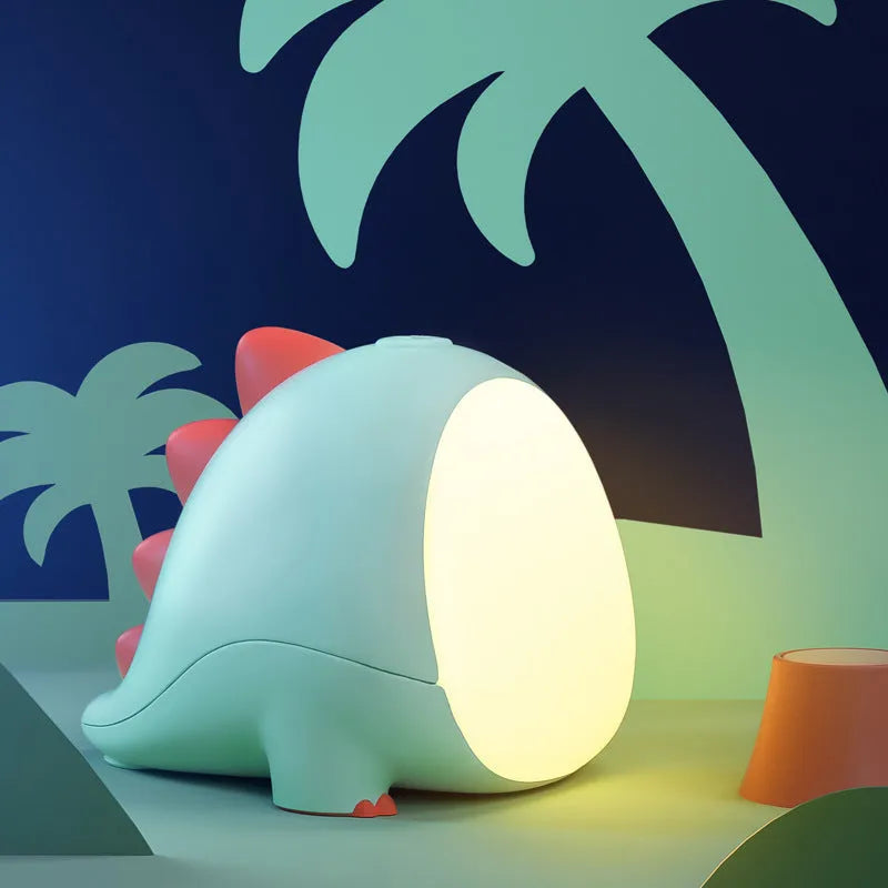 Green dinosaur silicone night light with USB cable, on a bedside table, showing warm light setting