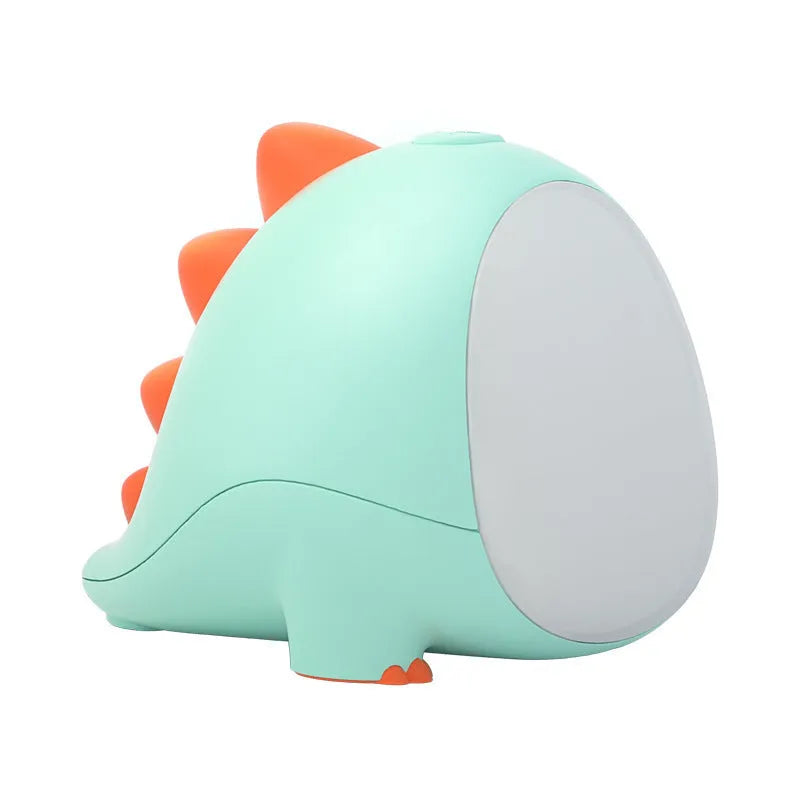 Green dinosaur silicone night light with USB cable, on a bedside table, showing warm light setting