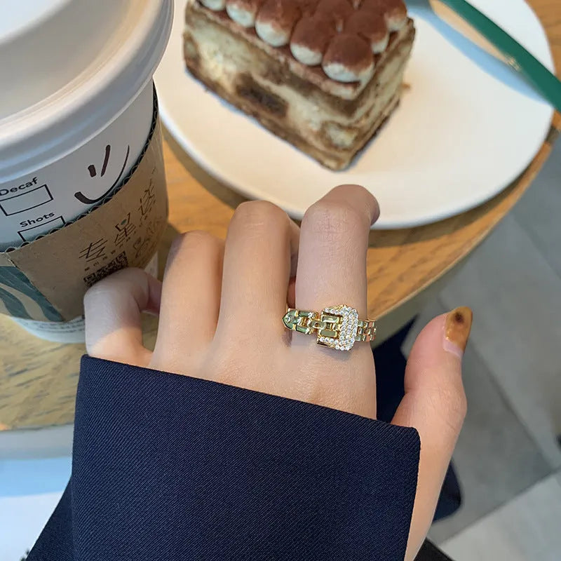 Gold adjustable belt buckle zircon ring with detachable metal chain on women's hand against light background