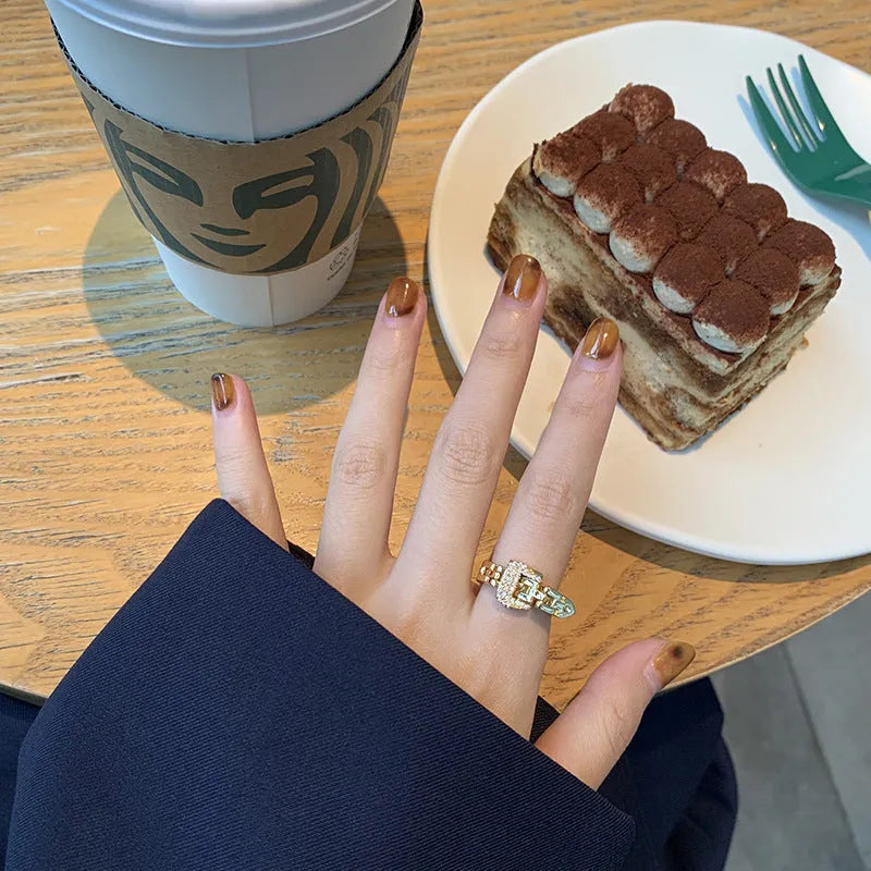 Gold adjustable belt buckle zircon ring with detachable metal chain on women's hand against light background