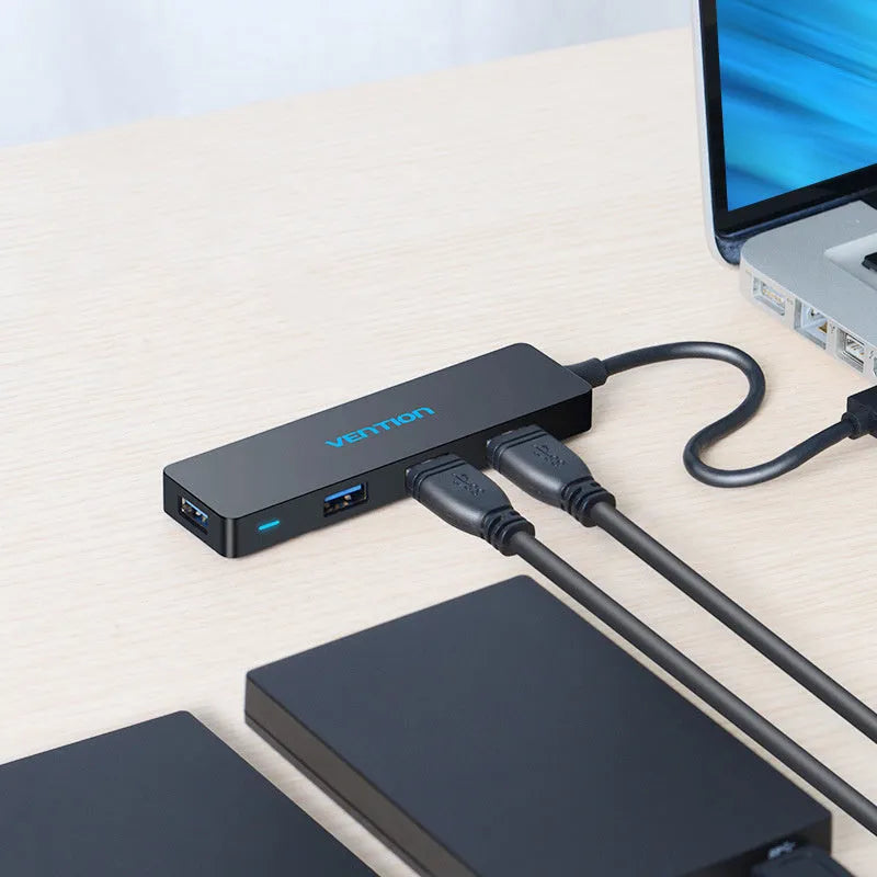 Black four-port USB 3.0 hub with a short attached cable on a desk.