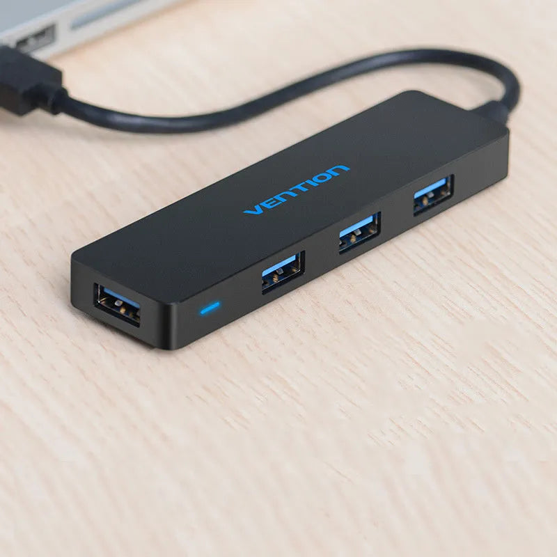 Black four-port USB 3.0 hub with a short attached cable on a desk.