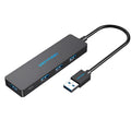 Black four-port USB 3.0 hub with a short attached cable on a desk.
