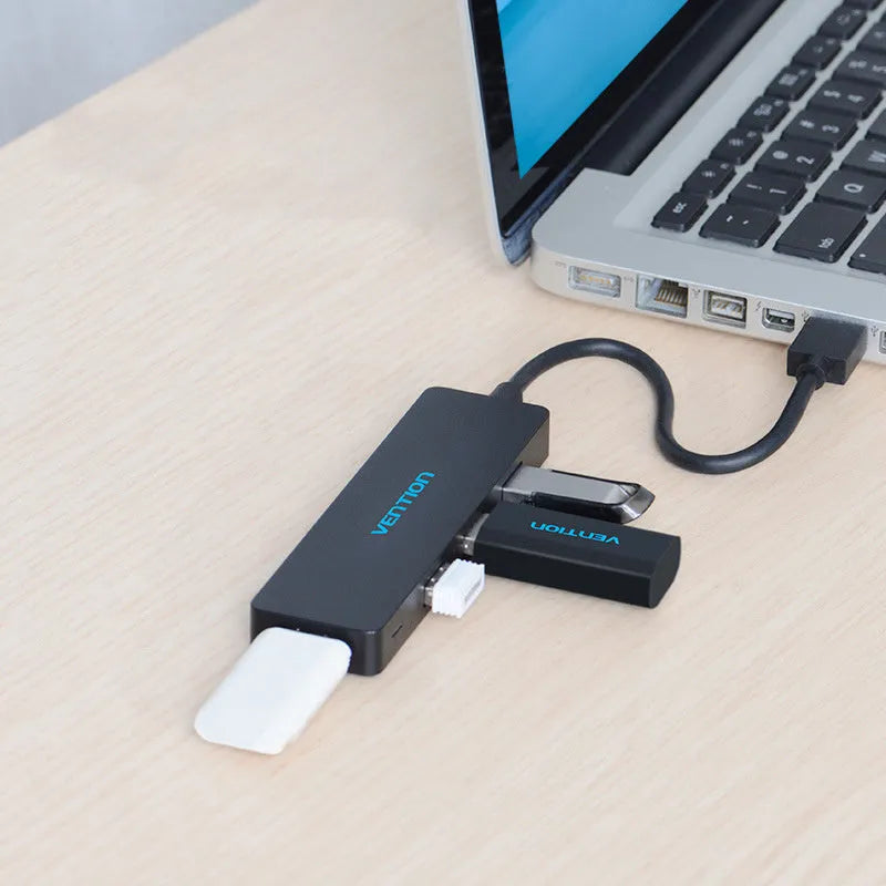Black four-port USB 3.0 hub with a short attached cable on a desk.