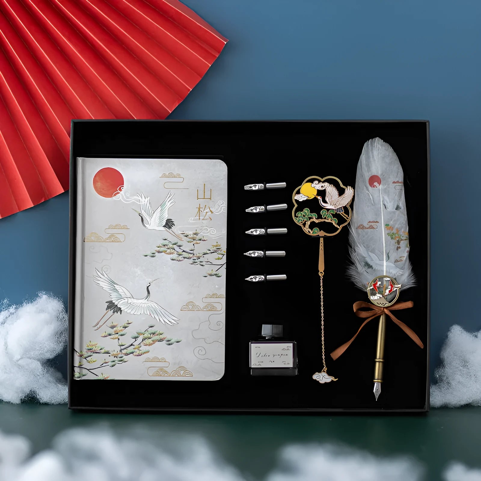 Chinese style metal feather pen with sheath and coloured feather collections next to a notebook.