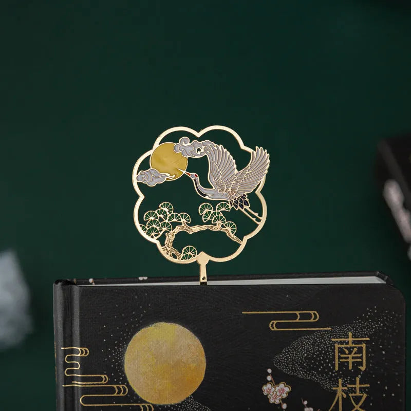 Chinese style metal feather pen with sheath and coloured feather collections next to a notebook.