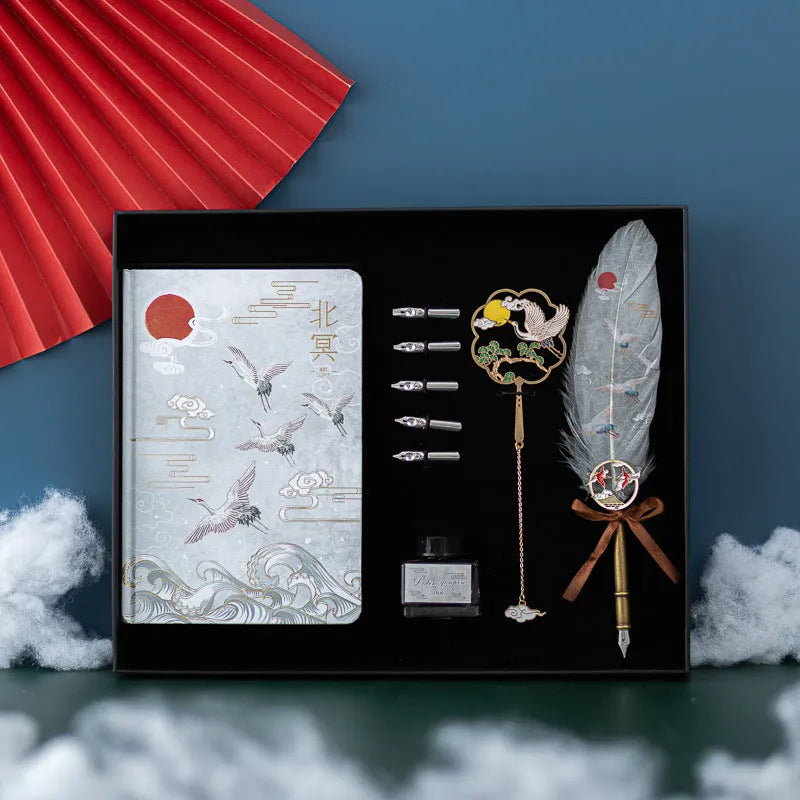 Chinese style metal feather pen with sheath and coloured feather collections next to a notebook.