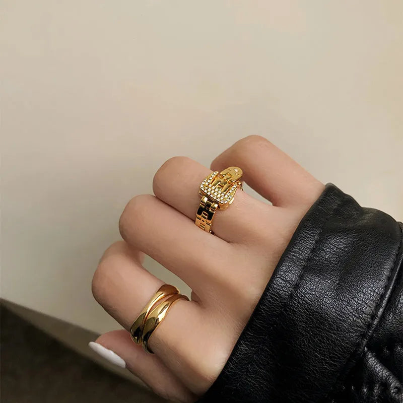 Gold adjustable belt buckle zircon ring with detachable metal chain on women's hand against light background