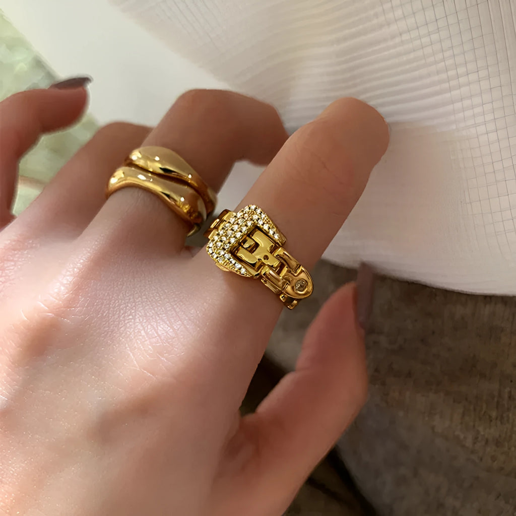 Gold adjustable belt buckle zircon ring with detachable metal chain on women's hand against light background