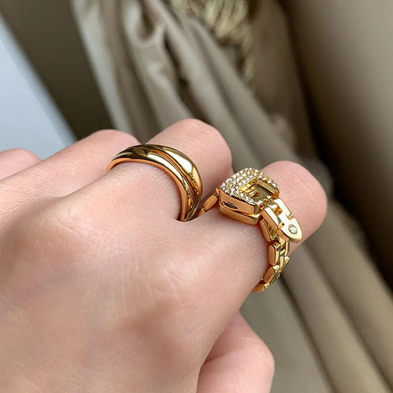 Gold adjustable belt buckle zircon ring with detachable metal chain on women's hand against light background