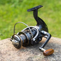 Telescopic carbon fibre fishing rod with spinning reel, solid wood handle, and metal wire cup on a rocky shore