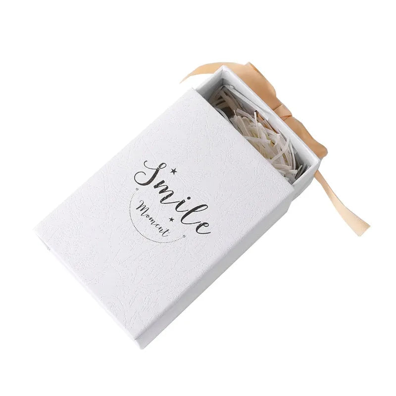 Small cardboard gift box with bronzing detail, handbag, and raffia tie in blue colour