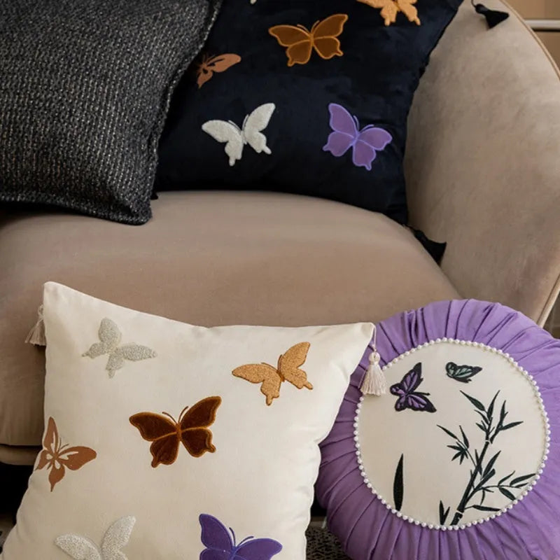 Square decorative cushion with Chinese butterfly embroidery in beige, black, and purple threads.