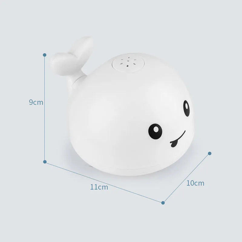 White and blue whale-shaped bath toy spraying water with LED lights on, floating in a baby bath
