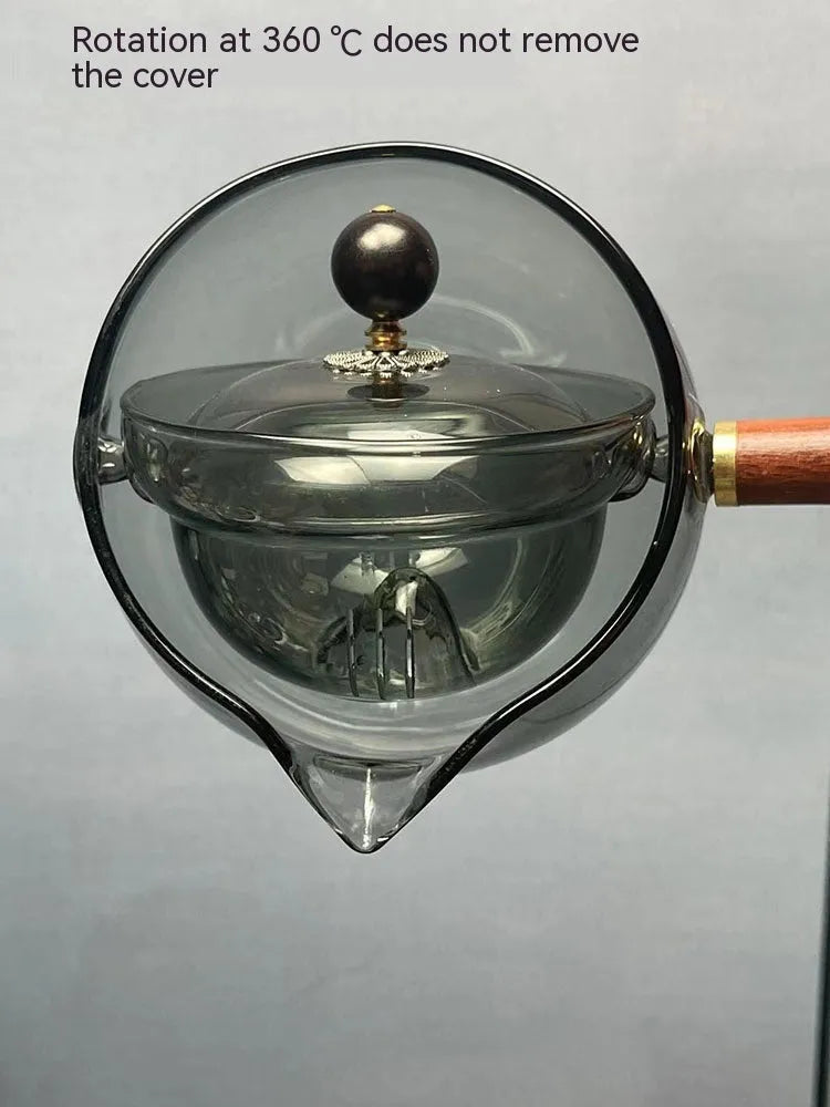 Transparent rotary glass teapot with wooden handle and built-in tea infuser on a table.