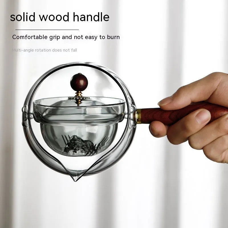 Transparent rotary glass teapot with wooden handle and built-in tea infuser on a table.