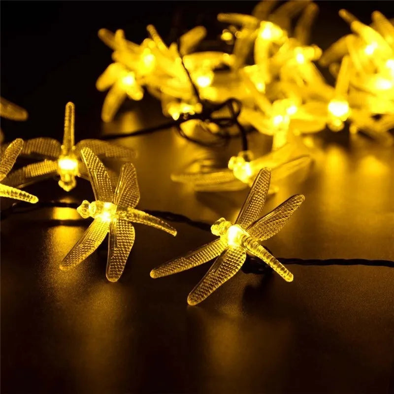 Outdoor solar LED dragonfly string lights with warm white bulbs on a 5-metre cable and a ground-spike solar panel.