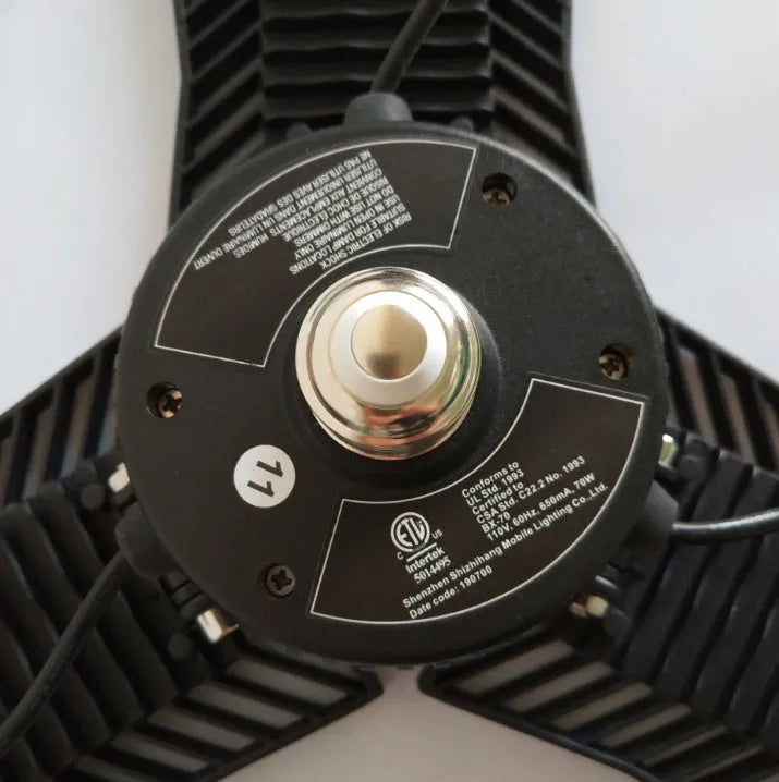 A foldable silver industrial LED garage lamp with a polycarbonate lens, shown in a workshop setting.