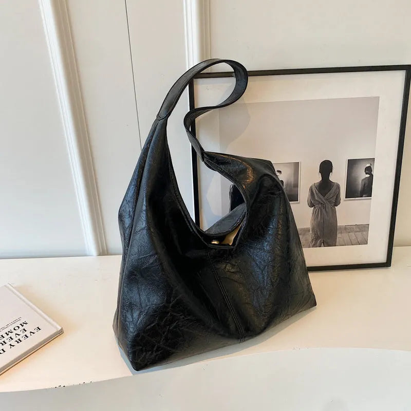 Soft black PU leather shoulder bag with large compartment and adjustable strap on a plain background.