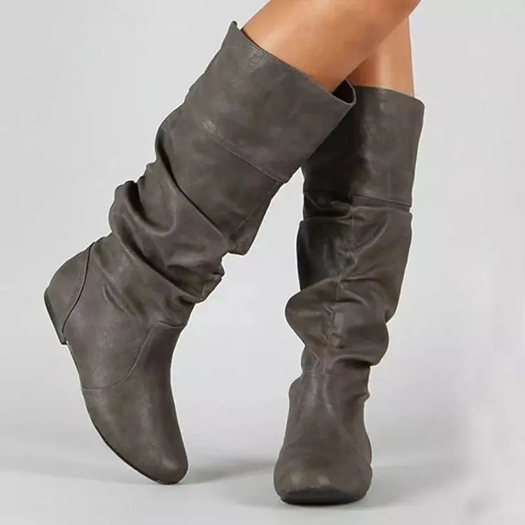 Women's black slip-on flat boots with a round toe and high cylinder shaft, showing the rubber sole.