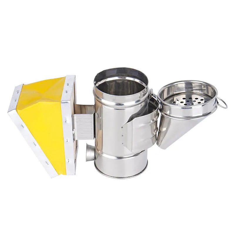 Stainless steel bee smoker with leather bellow on a wooden table against a blurred outdoor background