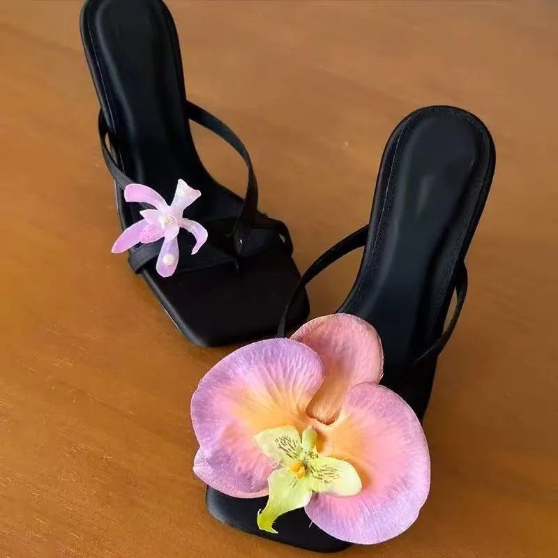 Women's black asymmetric floral high-heel sandals with a square toe and calf leather upper.