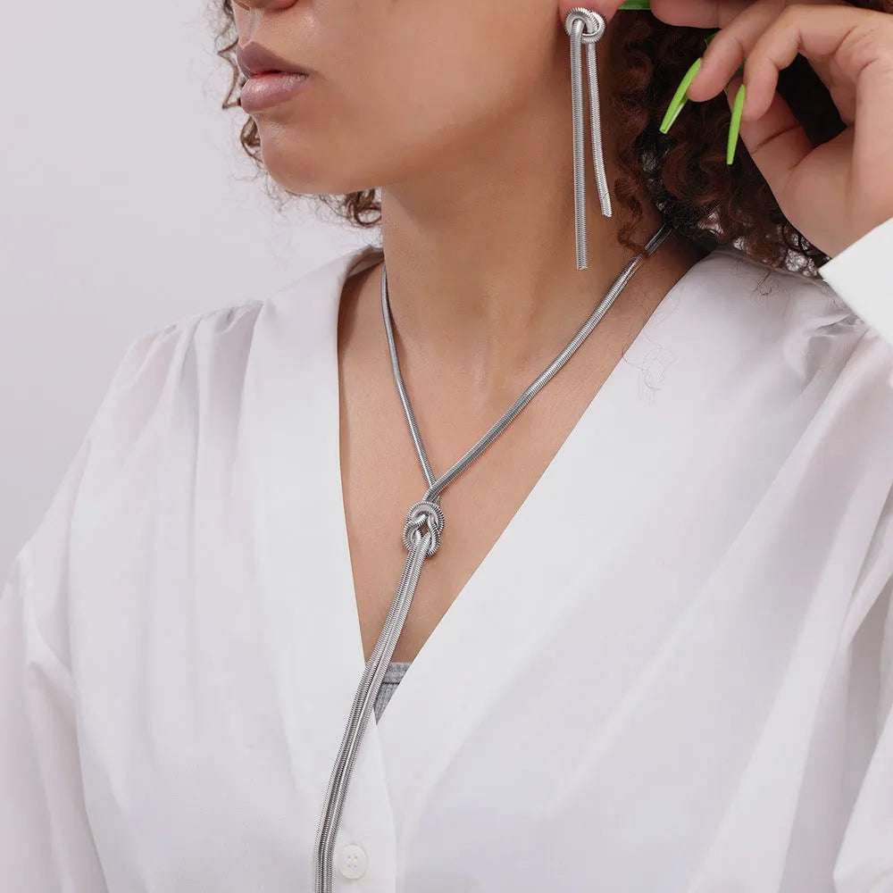 Gold long necklace with knotted tassel pendant and snake chain, shown with matching earrings.