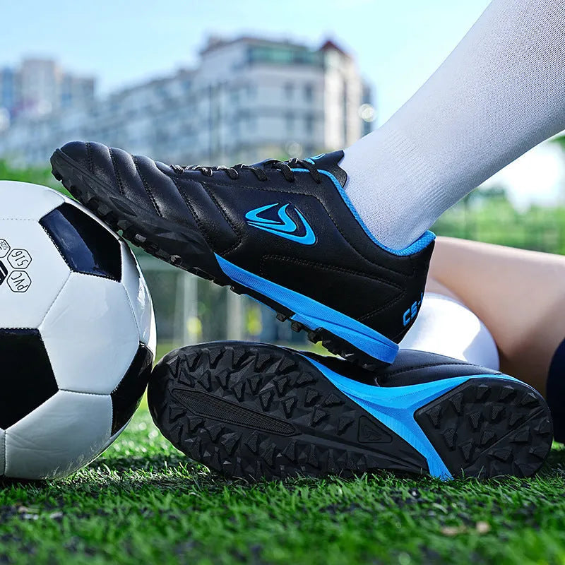 Low-top outdoor soccer shoes in a black and blue broken nails colourway on a turf background.