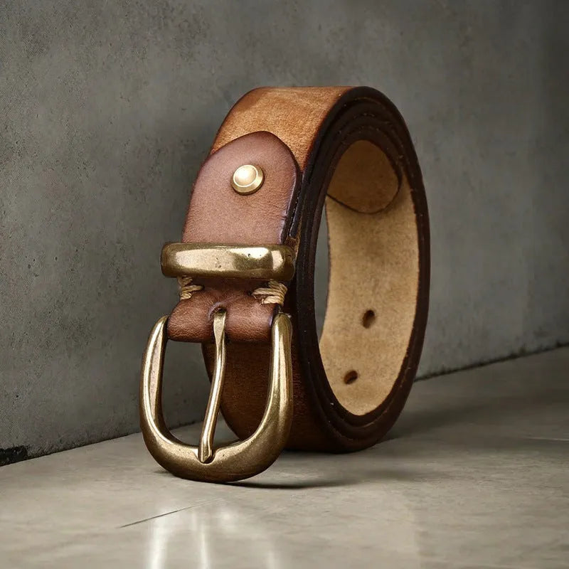 Men's black cattlehide leather jeans belt with a copper pin buckle on a wooden background.