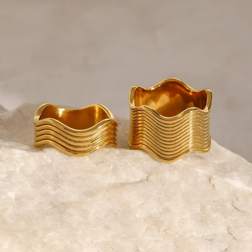 Silver and gold-tone stainless steel ring with a wide geometric wave design on a flat surface.