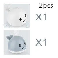 White and blue whale-shaped bath toy spraying water with LED lights on, floating in a baby bath