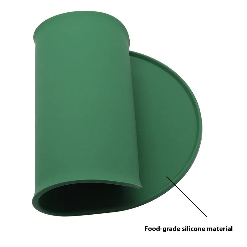 Green silicone cat feeding placemat on a floor next to a food bowl.