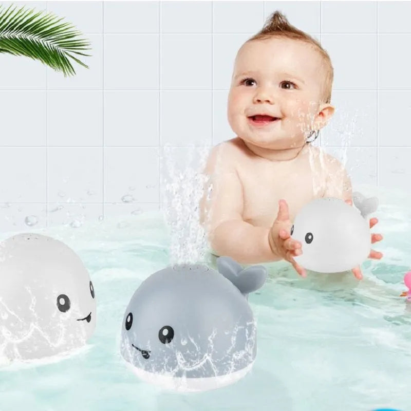 White and blue whale-shaped bath toy spraying water with LED lights on, floating in a baby bath