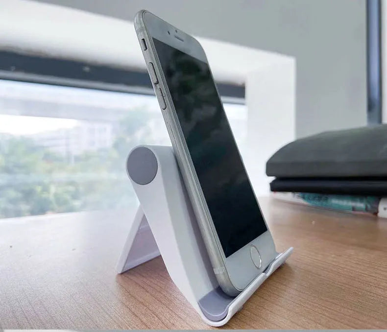 Black PE folding stand holding a smartphone at an angle on a wooden table.