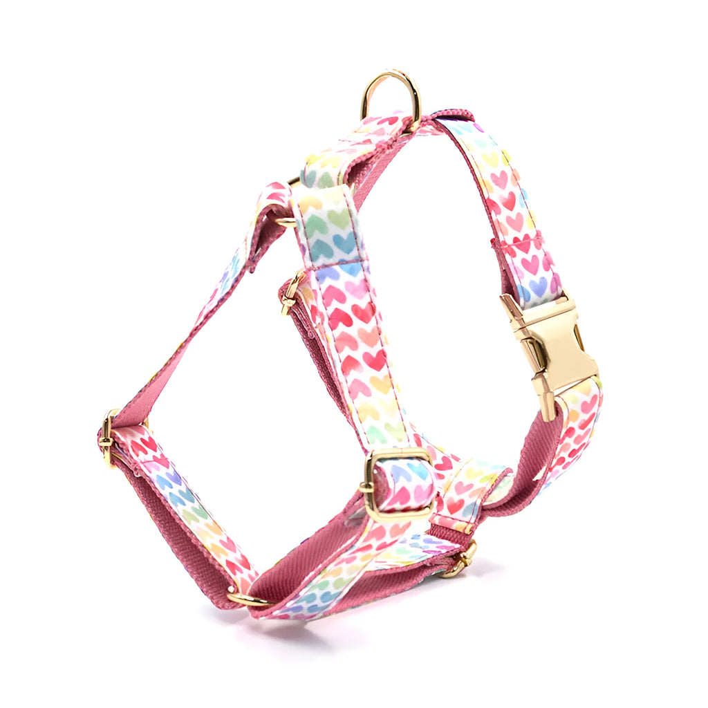 Pink dog harness with a gold buckle and colourful heart-shaped stone decoration on an adjustable polyester strap.