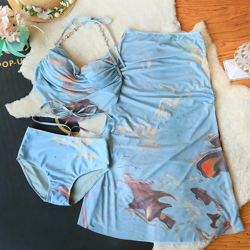 Women's blue printed bikini set with triangle top, bikini pants, and matching skirt laid flat.