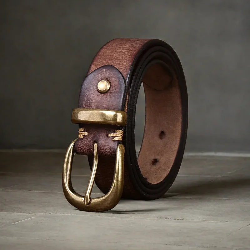 Men's black cattlehide leather jeans belt with a copper pin buckle on a wooden background.